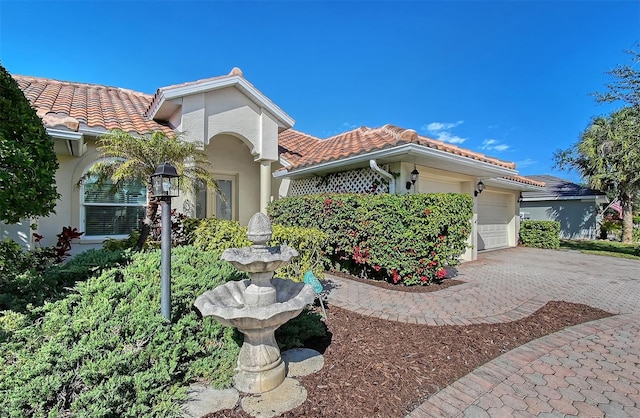 mediterranean / spanish house featuring decorative driveway, a tile roof, an attached garage, and stucco siding