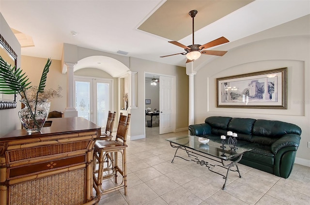 living area featuring arched walkways, light tile patterned floors, a ceiling fan, french doors, and decorative columns