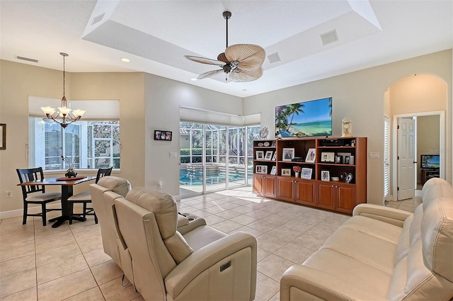 tiled living room with a raised ceiling and ceiling fan with notable chandelier