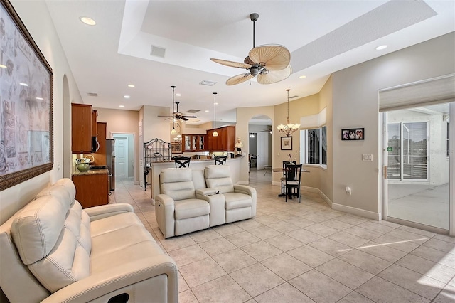 living room featuring light tile patterned floors, a tray ceiling, and ceiling fan with notable chandelier