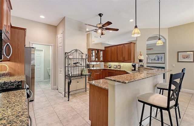 kitchen with stone counters, a peninsula, a breakfast bar, a sink, and tasteful backsplash