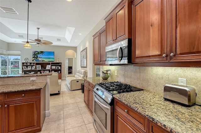 kitchen featuring light stone countertops, decorative light fixtures, stainless steel appliances, and a raised ceiling