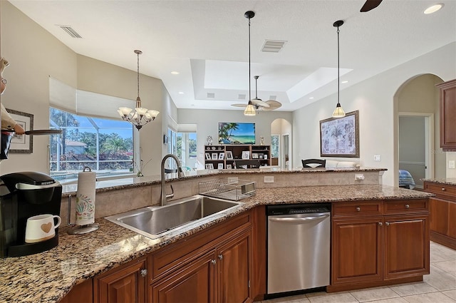 kitchen featuring ceiling fan with notable chandelier, dishwasher, sink, light stone counters, and a tray ceiling