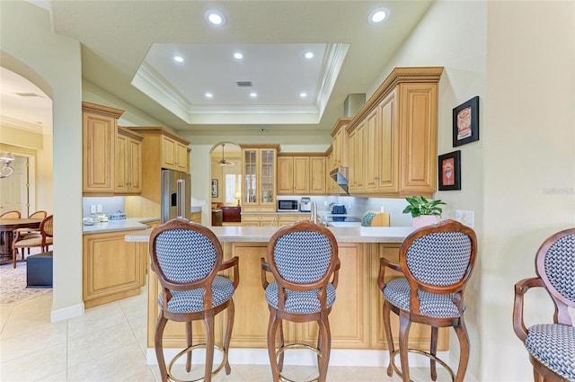 kitchen with crown molding, appliances with stainless steel finishes, a tray ceiling, light tile patterned flooring, and light brown cabinetry