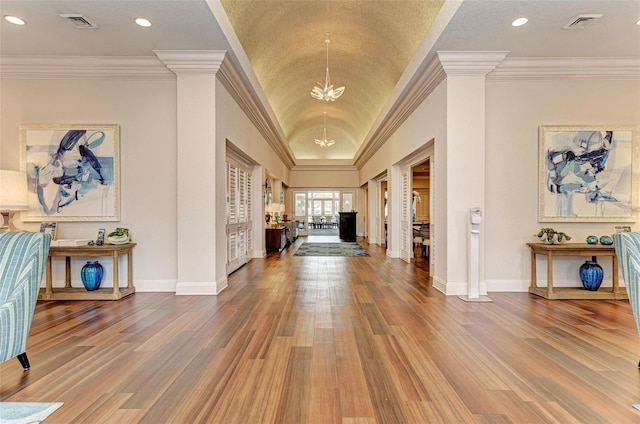 entrance foyer with an inviting chandelier, hardwood / wood-style floors, ornamental molding, and ornate columns