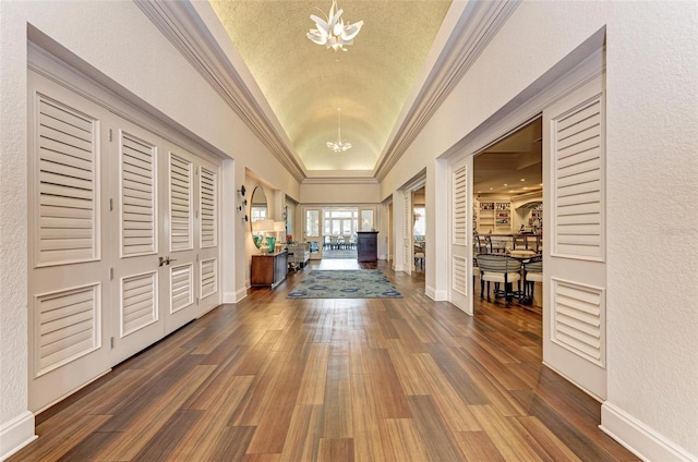 entrance foyer featuring an inviting chandelier, dark hardwood / wood-style flooring, vaulted ceiling, and crown molding