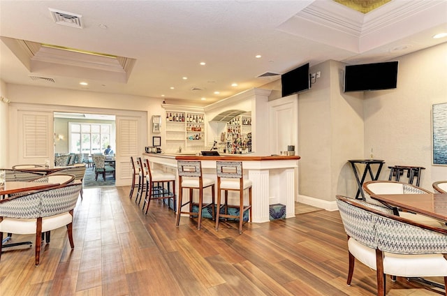 interior space with hardwood / wood-style flooring, bar area, crown molding, and a raised ceiling