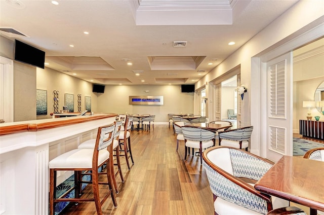 dining space with a tray ceiling, light hardwood / wood-style flooring, ornamental molding, and bar area