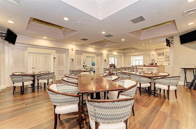 dining room with a raised ceiling, ornamental molding, a textured ceiling, and light wood-type flooring