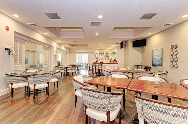 dining space with a raised ceiling, crown molding, a textured ceiling, and light wood-type flooring