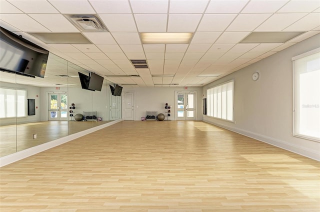 exercise room with light hardwood / wood-style flooring, a drop ceiling, and french doors