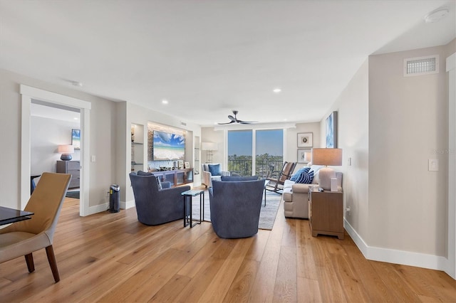 living room with built in shelves, light hardwood / wood-style flooring, and ceiling fan