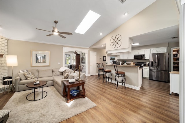 living room featuring high vaulted ceiling, a skylight, ceiling fan, and wood finished floors