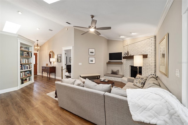 living area featuring vaulted ceiling with skylight, ceiling fan, wood finished floors, crown molding, and a brick fireplace