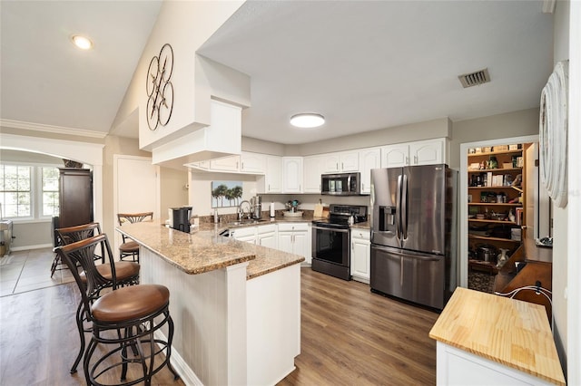 kitchen featuring arched walkways, a breakfast bar area, stainless steel appliances, white cabinets, and a peninsula