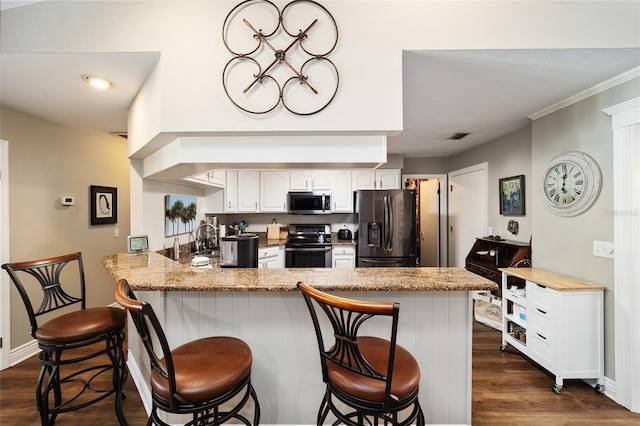 kitchen with a peninsula, a breakfast bar area, appliances with stainless steel finishes, and dark wood-type flooring