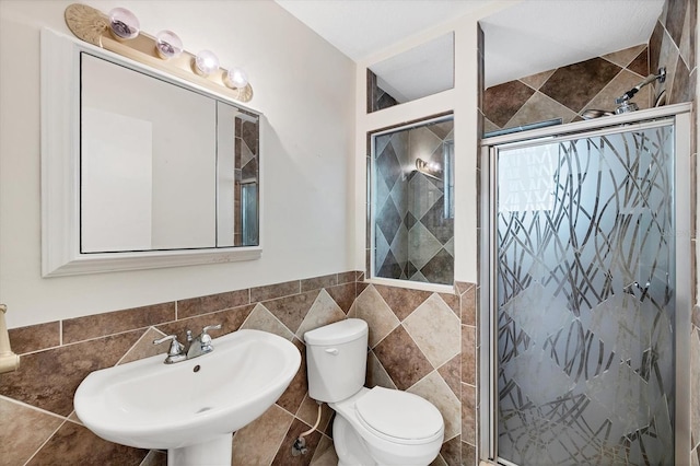 bathroom featuring toilet, a shower with shower door, sink, and tile walls