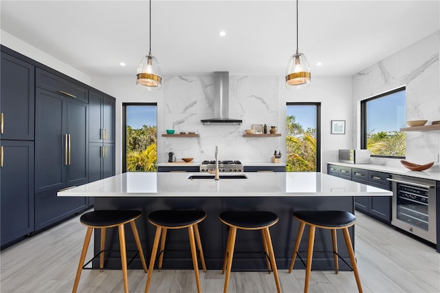 kitchen featuring a kitchen island with sink, backsplash, hanging light fixtures, wine cooler, and wall chimney exhaust hood