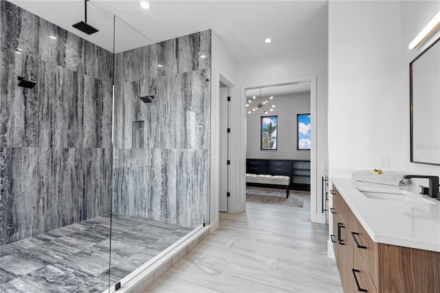 bathroom featuring an inviting chandelier, tiled shower, and vanity