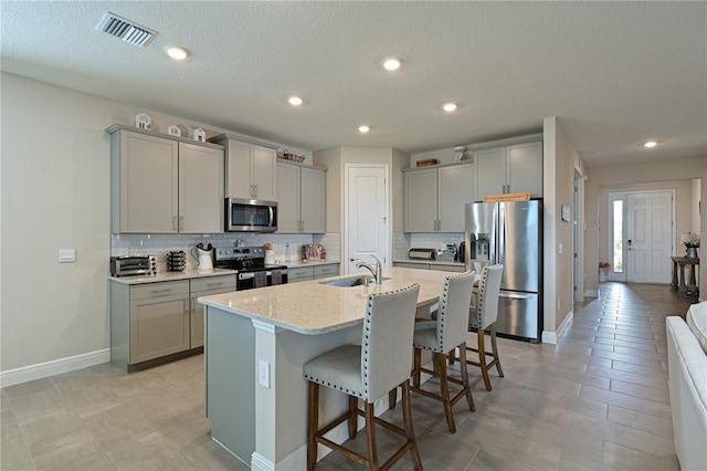 kitchen featuring sink, gray cabinets, a breakfast bar, appliances with stainless steel finishes, and a kitchen island with sink