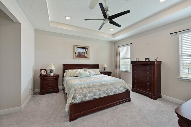 bedroom with multiple windows, a tray ceiling, light carpet, and a textured ceiling