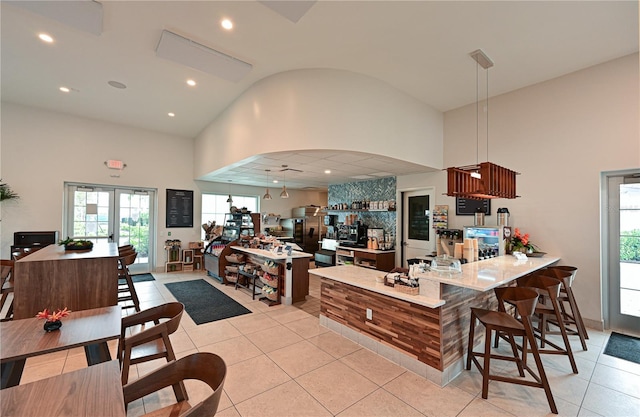 kitchen with light tile patterned flooring, kitchen peninsula, high vaulted ceiling, and french doors