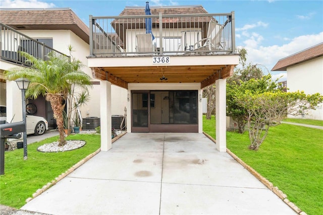 view of exterior entry featuring a carport, a balcony, central air condition unit, and a lawn