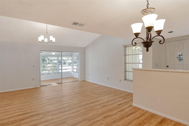 unfurnished living room featuring an inviting chandelier, light hardwood / wood-style flooring, a textured ceiling, and vaulted ceiling