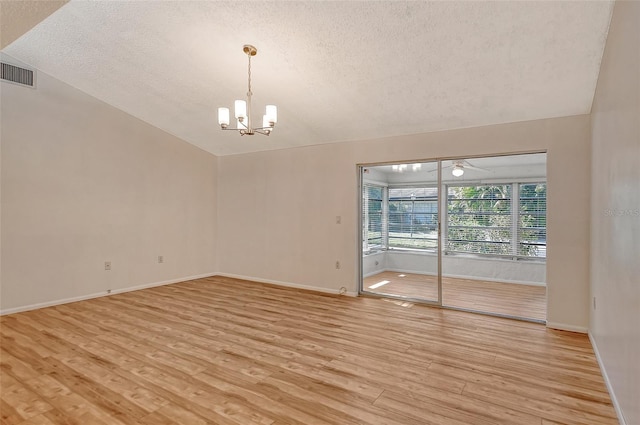 unfurnished room with a textured ceiling, vaulted ceiling, a chandelier, and light wood-type flooring