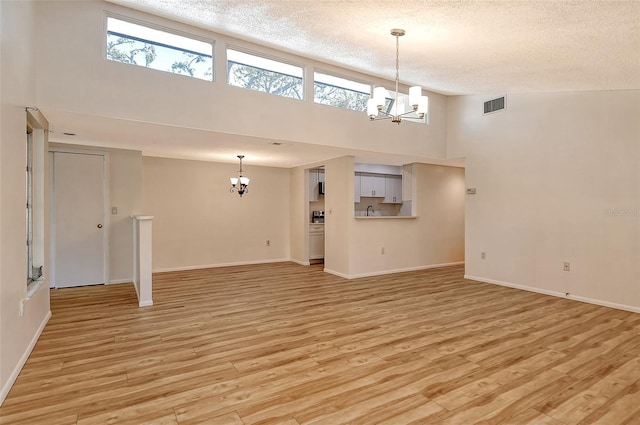 unfurnished living room featuring high vaulted ceiling, light wood-type flooring, and a notable chandelier