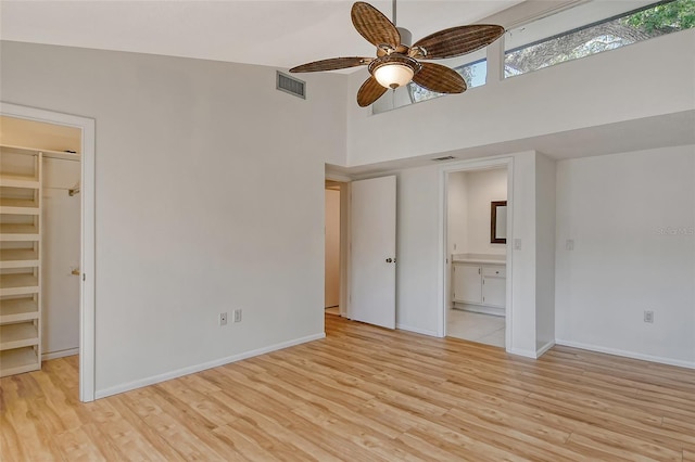 unfurnished bedroom featuring a high ceiling, a spacious closet, connected bathroom, and light wood-type flooring