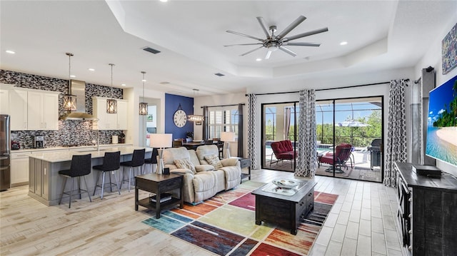 living room featuring ceiling fan, a healthy amount of sunlight, a raised ceiling, and light wood-type flooring