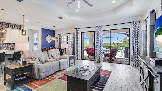 living room with ceiling fan, a raised ceiling, and light wood-type flooring