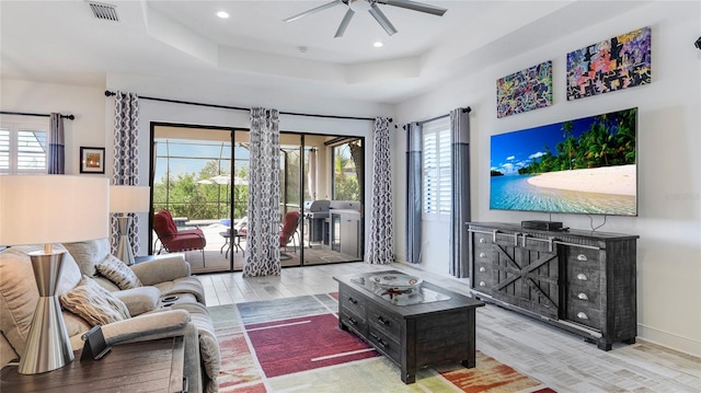 living room with a tray ceiling, ceiling fan, and light wood-type flooring