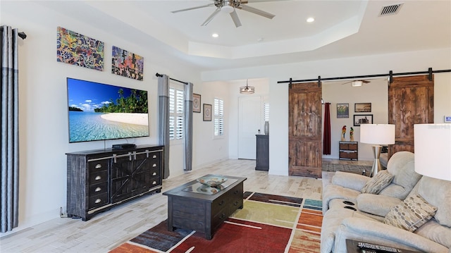 living room with a raised ceiling, a barn door, ceiling fan, and light hardwood / wood-style flooring