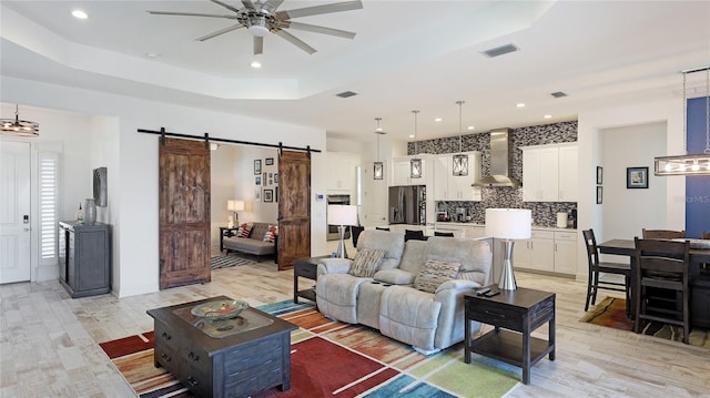 living room with a tray ceiling, a barn door, and light hardwood / wood-style floors