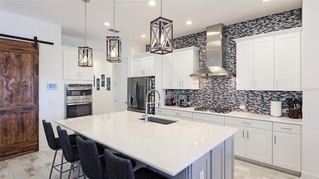 kitchen featuring a kitchen island with sink, sink, white cabinets, and wall chimney exhaust hood