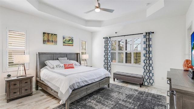 bedroom with multiple windows, a raised ceiling, ceiling fan, and light wood-type flooring