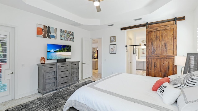 bedroom with ceiling fan, connected bathroom, a barn door, and a raised ceiling