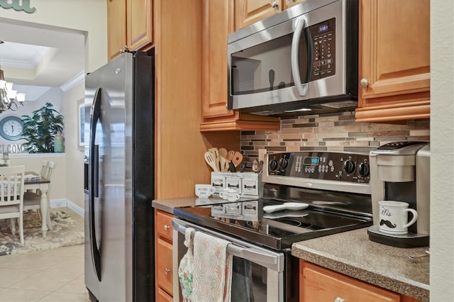 kitchen featuring crown molding, appliances with stainless steel finishes, decorative backsplash, a raised ceiling, and a chandelier