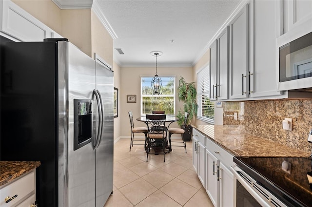 kitchen featuring crown molding, appliances with stainless steel finishes, hanging light fixtures, tasteful backsplash, and dark stone counters