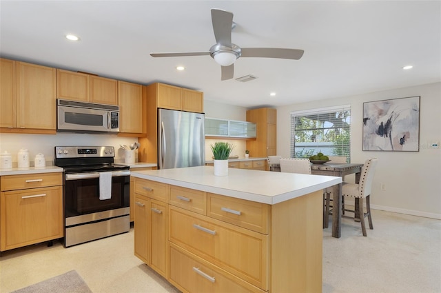 kitchen with light brown cabinetry, light carpet, a kitchen island, ceiling fan, and stainless steel appliances