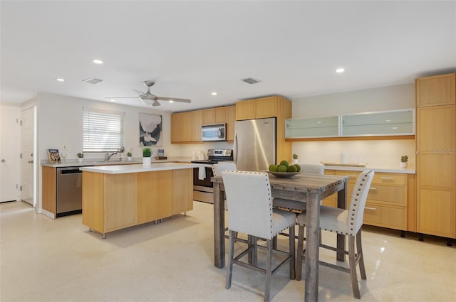 kitchen with ceiling fan, appliances with stainless steel finishes, sink, and a kitchen island