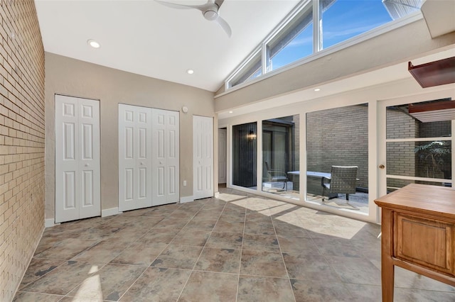 unfurnished bedroom featuring ceiling fan, high vaulted ceiling, brick wall, access to outside, and multiple closets