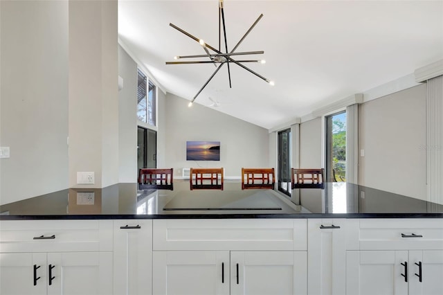 kitchen featuring cooktop, vaulted ceiling, a chandelier, and white cabinets