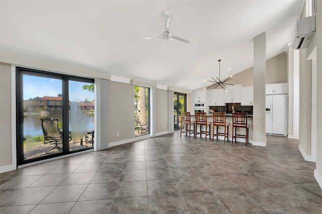 interior space with a water view, ceiling fan with notable chandelier, an AC wall unit, and high vaulted ceiling