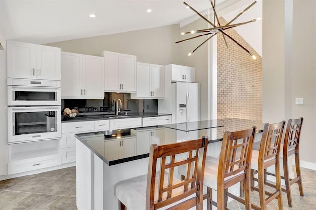 kitchen featuring white cabinetry, white appliances, lofted ceiling, and a kitchen bar