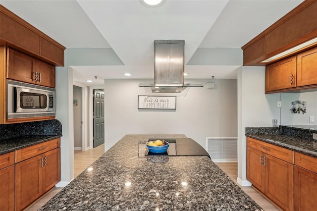 kitchen with stainless steel microwave, island range hood, and dark stone countertops