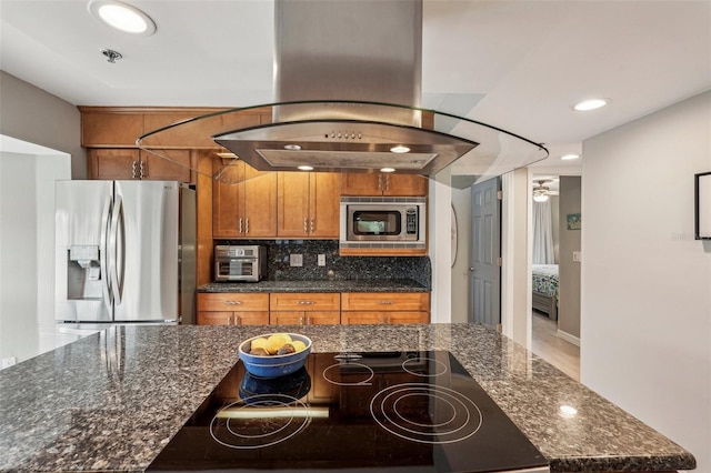 kitchen with appliances with stainless steel finishes, island range hood, decorative backsplash, and dark stone counters