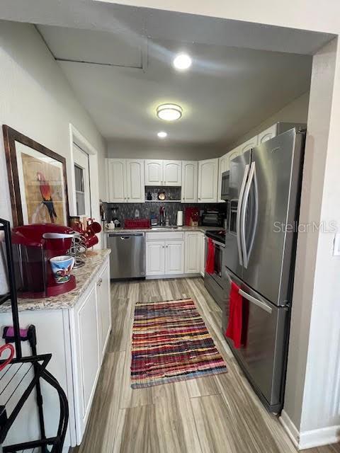 kitchen with sink, light wood-type flooring, white cabinets, stainless steel appliances, and backsplash